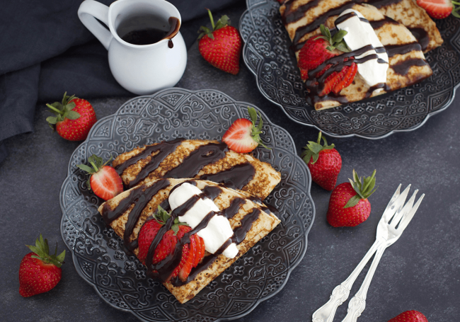 Glutenfria pannkakor med fiberhusk serverade med grädde, jordgubbar och smält choklad